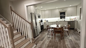 A spacious kitchen with white cabinets, a stainless steel refrigerator, and a wooden dining table. - Nisswa Lake Hubert Cabin on Paul Bunyan Trail ~In the heart of Brainerd Lakes~ (Nisswa)