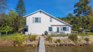 A two-story white house with a front porch, a garage, and a small driveway leading to a dock over water. - Nisswa Lake Hubert Cabin on Paul Bunyan Trail ~In the heart of Brainerd Lakes~ (Nisswa)