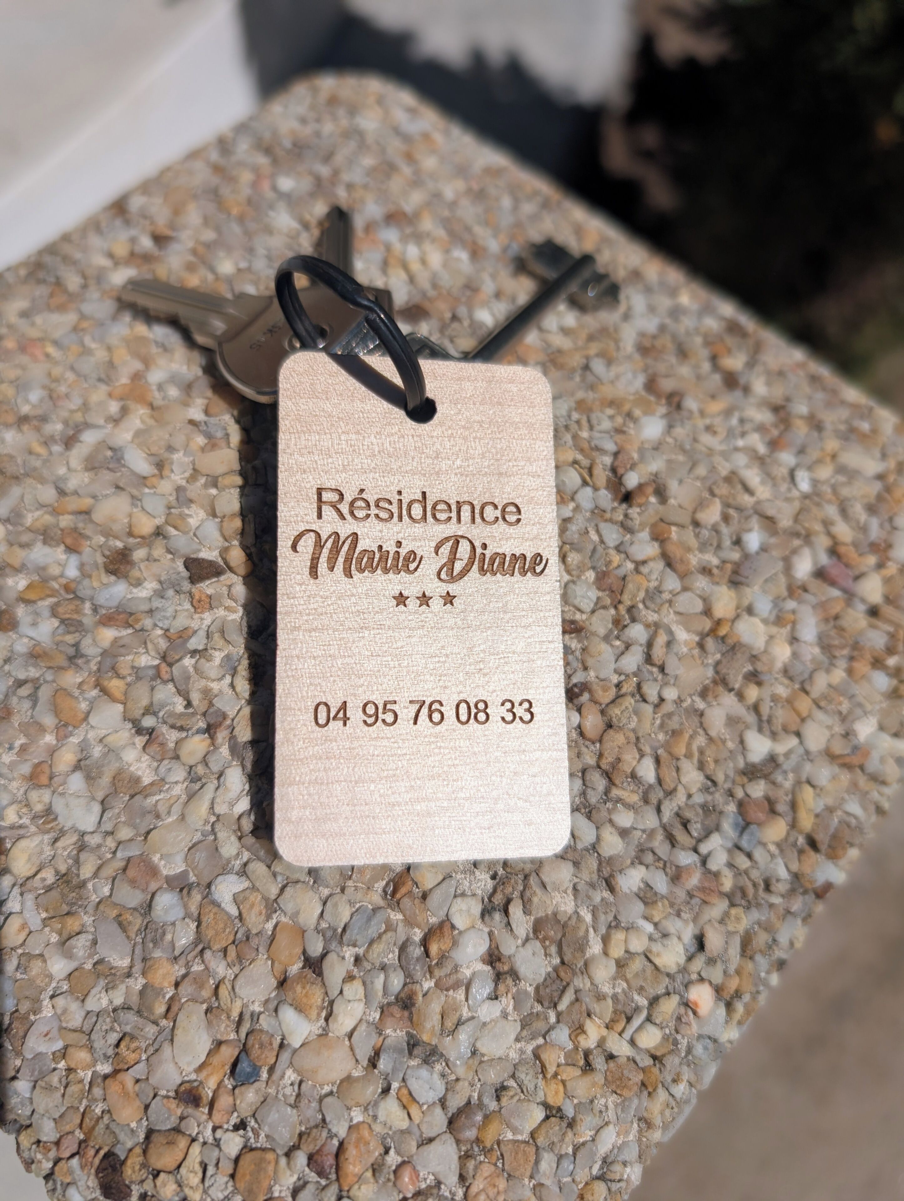 A tag with 'Résidence Marie Diane' and a phone number on a pebble-textured surface.