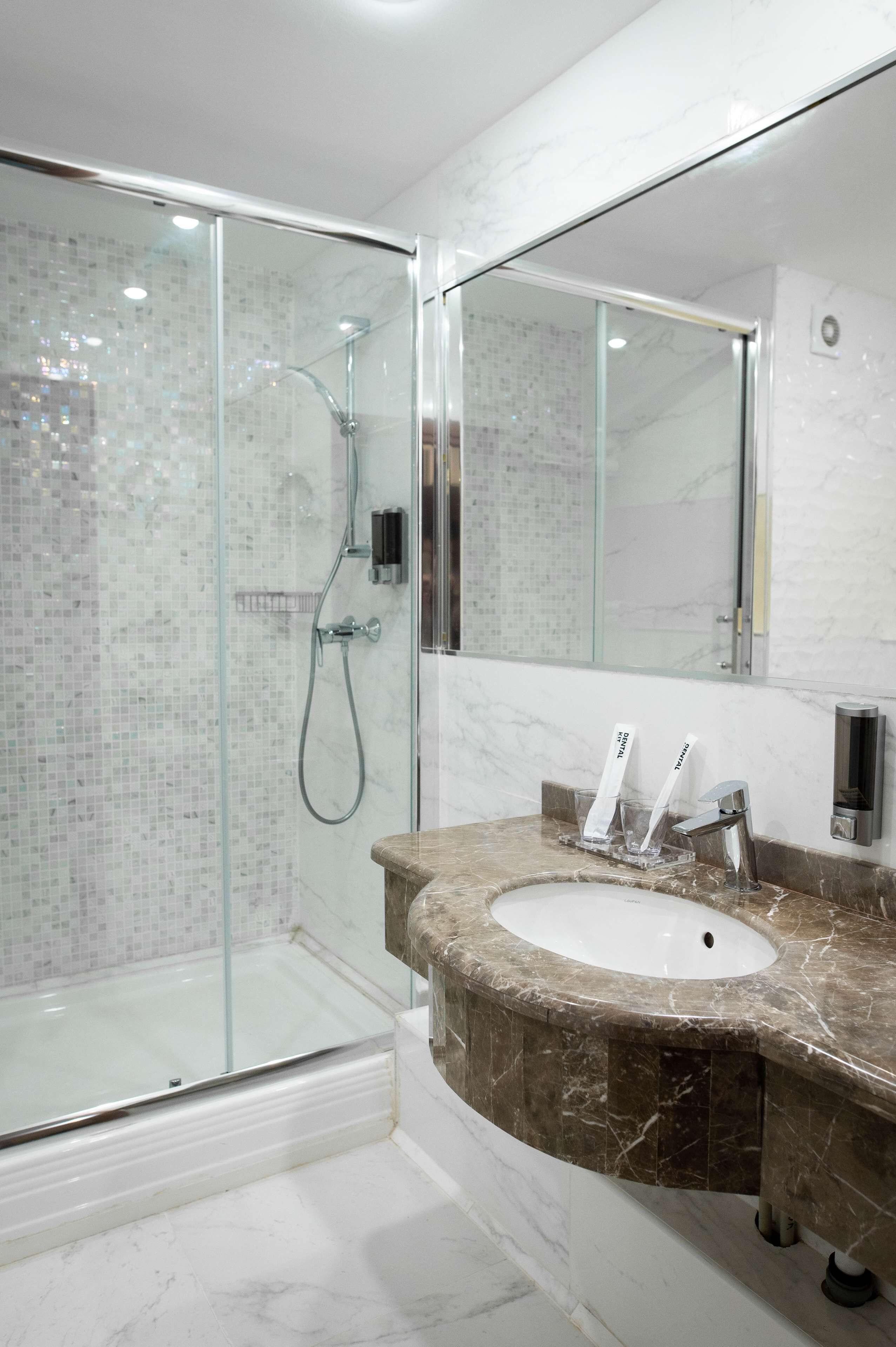 A modern bathroom with a glass-enclosed shower, a marble sink, and a large mirror.