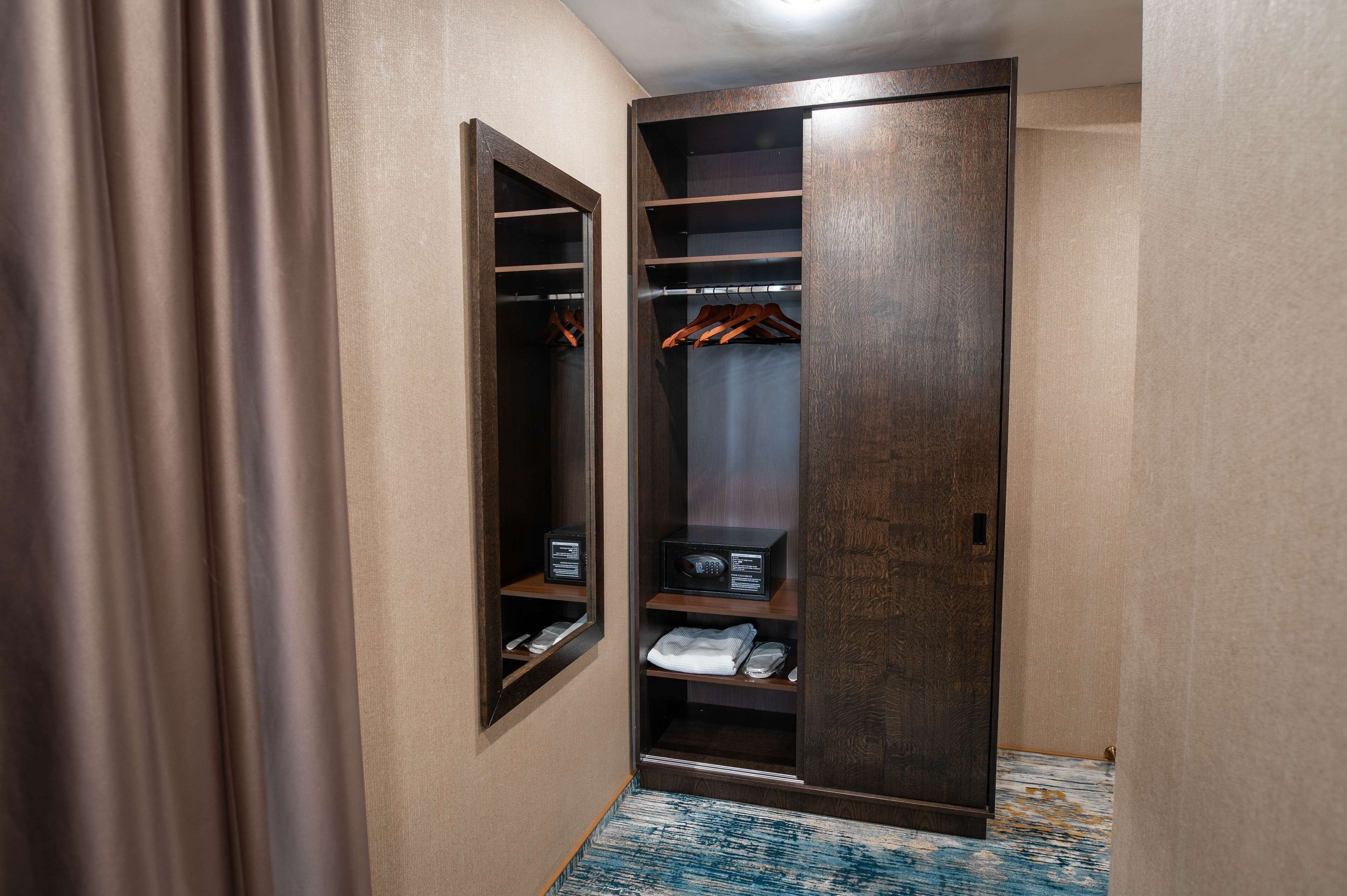 Un dressing avec des étagères en bois et un espace pour suspendre les vêtements, un petit bureau avec une chaise, et un tapis bleu à motifs sur le sol.