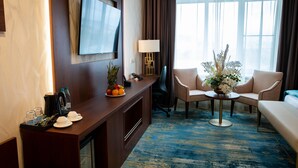 A hotel room with a wooden desk, a flat-screen TV, a sofa, and a large window with curtains. - Best Western Plus Oskemen (Oskemen)
