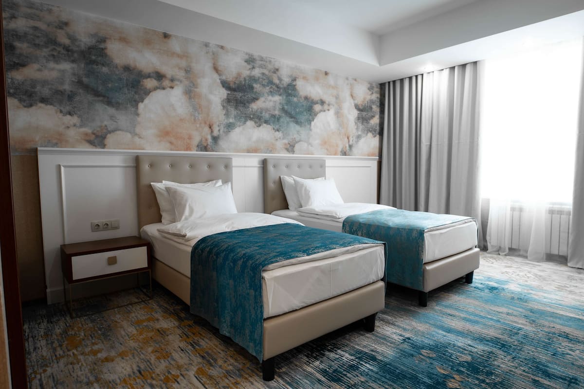 A hotel room with two beds, a marble wall, and a large window with curtains.