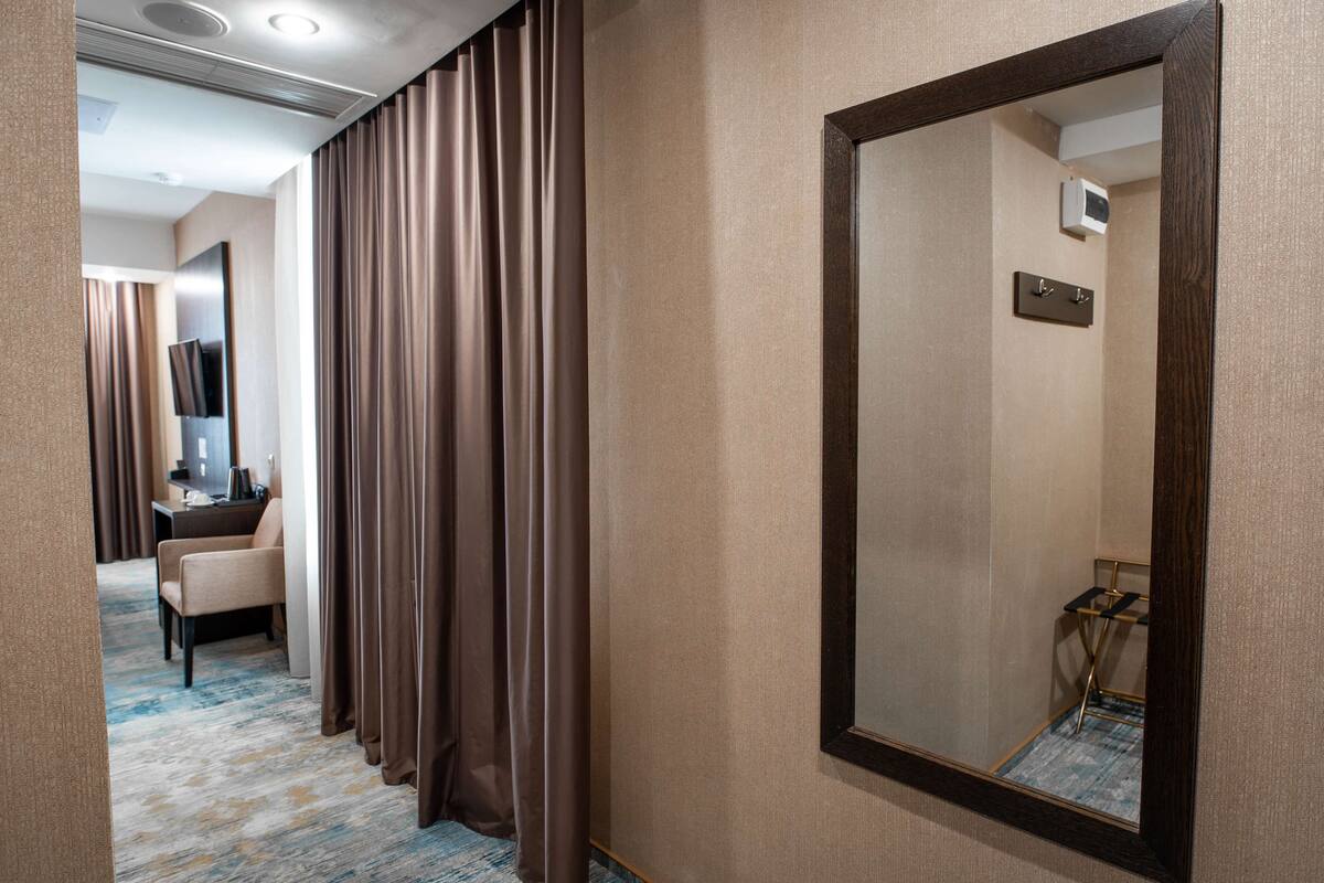 A hotel room with a large mirror, a desk with a chair, and a television.