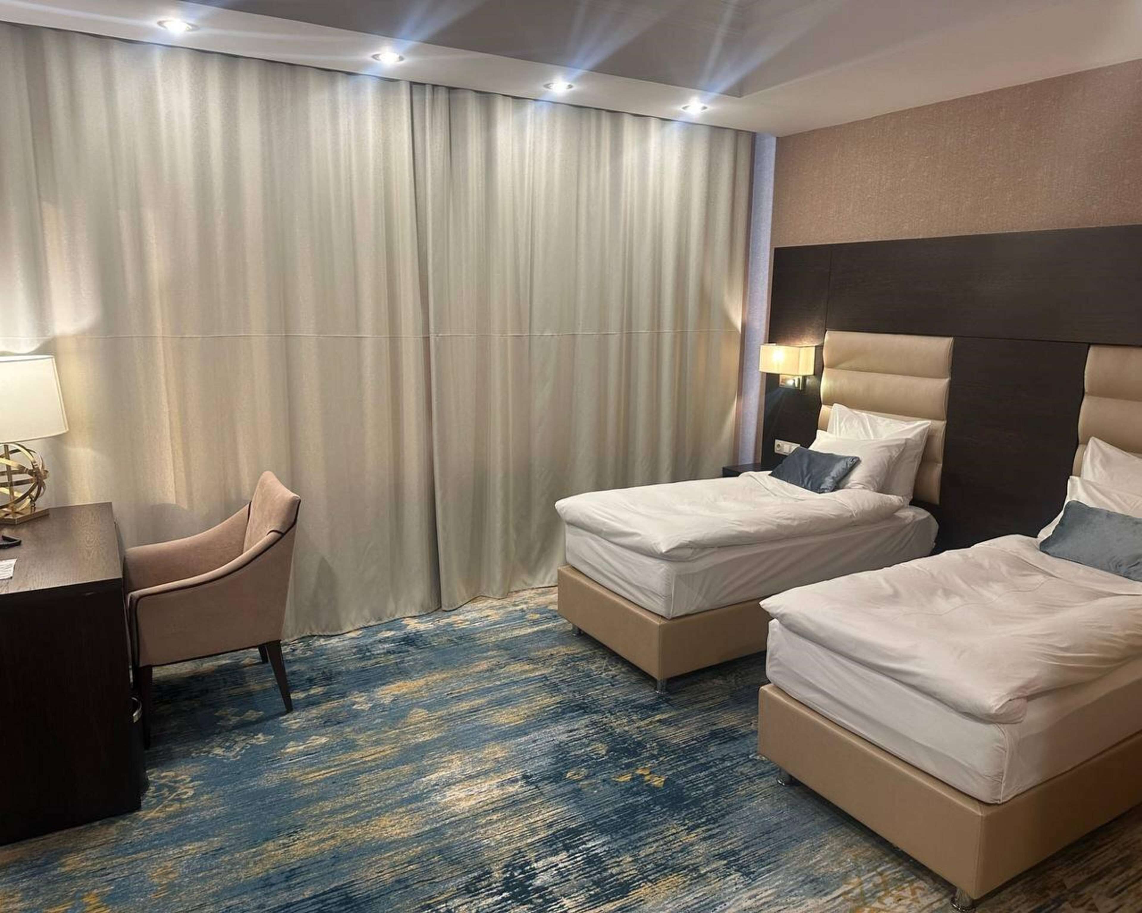 Een hotelkamer met twee bedden, een bureau, een stoel en een groot raam met gordijnen.