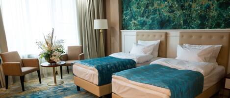 A hotel room with two beds, a sitting area with a chair and a small table, and a large abstract painting on the wall.