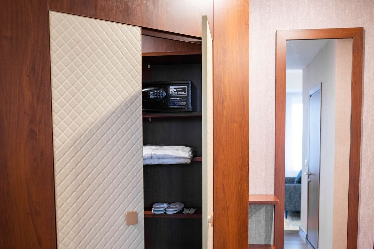 A walk-in closet with wooden doors and shelves, a microwave, and a mirror on the wall.