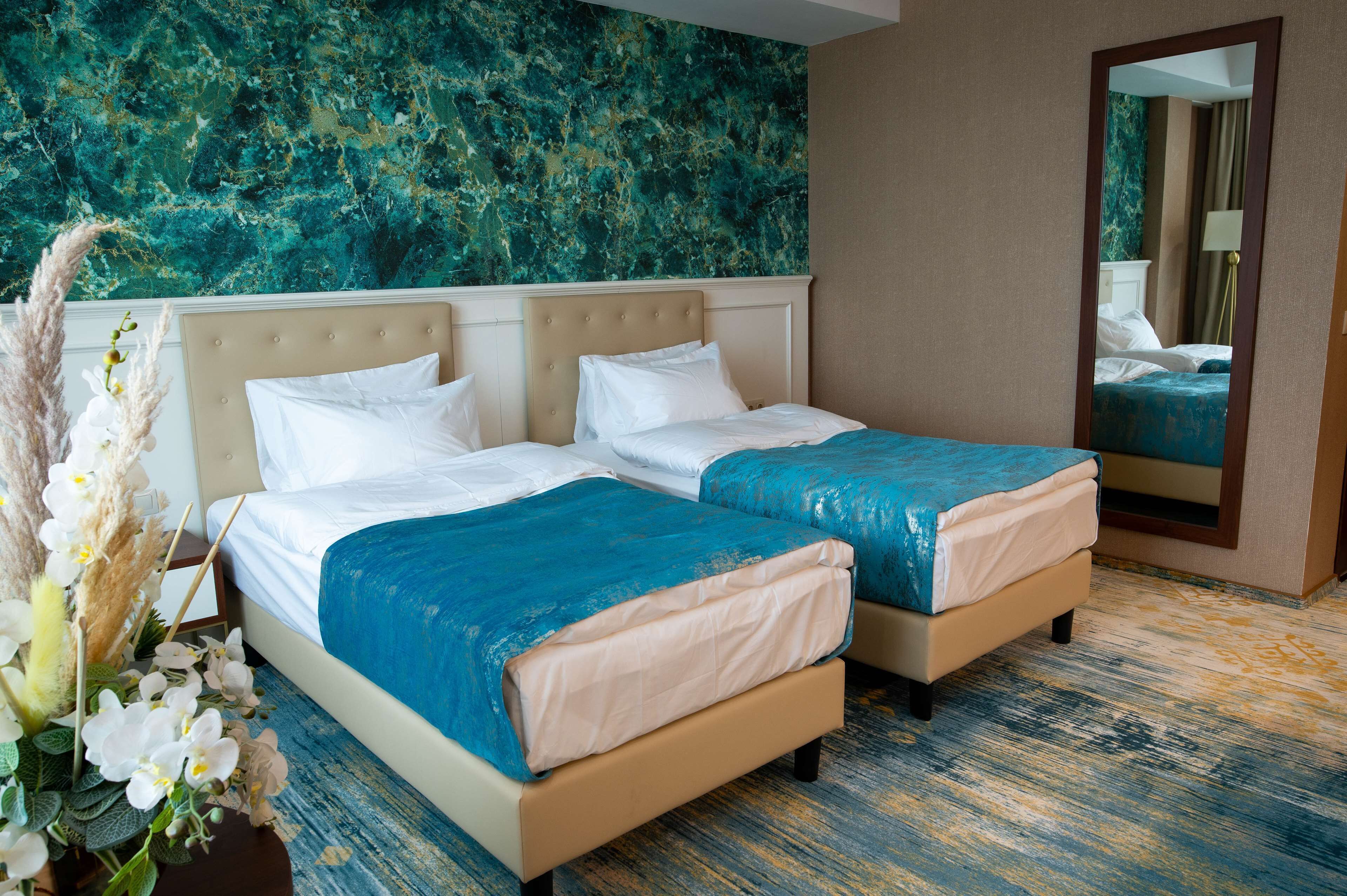 Habitación de hotel con dos camas, una pared de mármol, un espejo y un arreglo floral.