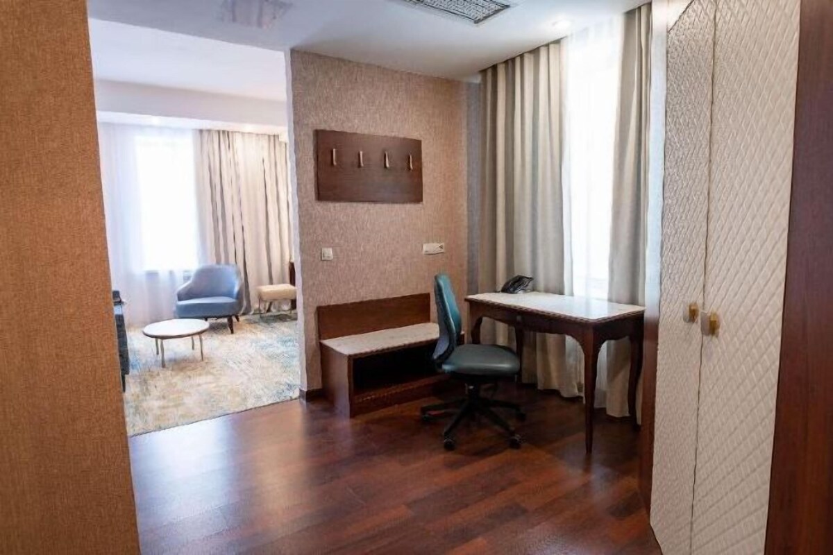 Une chambre d’hôtel avec un plancher en bois, un bureau, une chaise, un banc et une armoire.