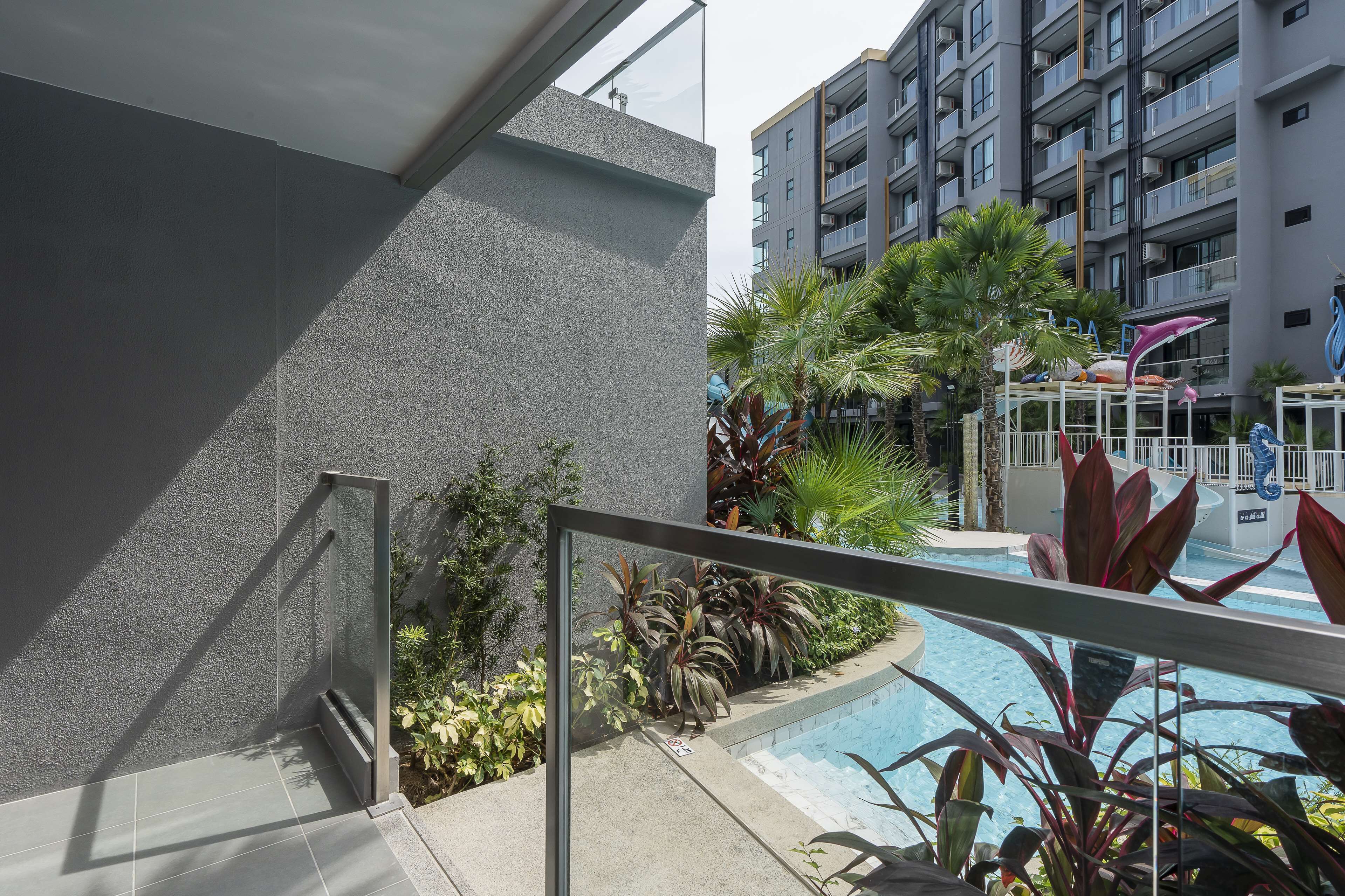 Un edificio moderno con zona de piscina, rodeado de plantas variadas y una barandilla de vidrio.