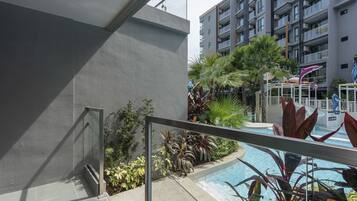 Un edificio moderno con zona de piscina, rodeado de plantas variadas y una barandilla de vidrio.
