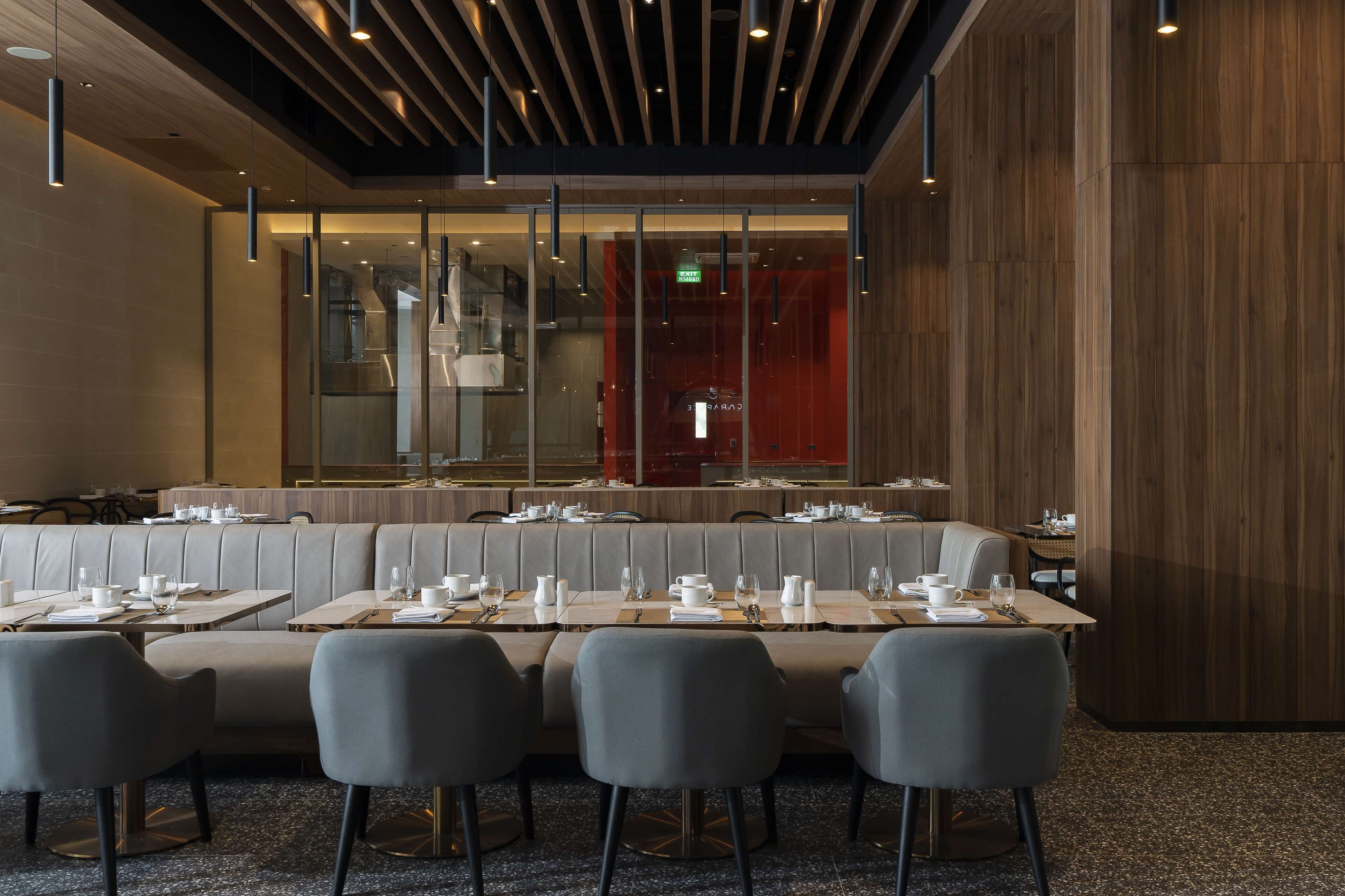En modern restaurang med ett långt, gemensamt bord, bekväma sittplatser och en vägg som är accentuerad med trä.