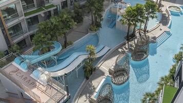 Relax by the infinity pool with multiple slides and water features, surrounded by lush greenery and palm trees.