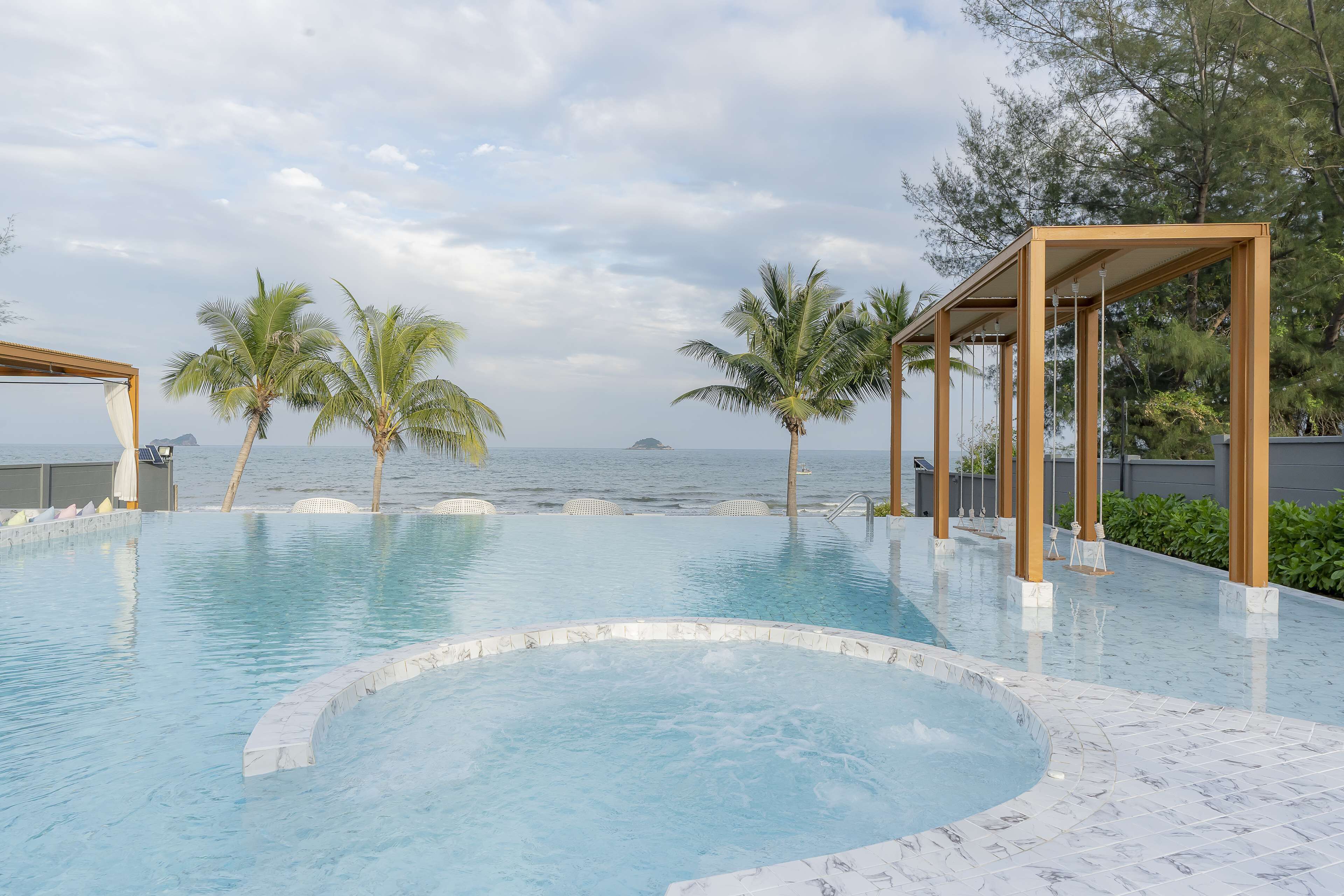 A swimming pool with a view of the sea, surrounded by palm trees and wooden pergolas.