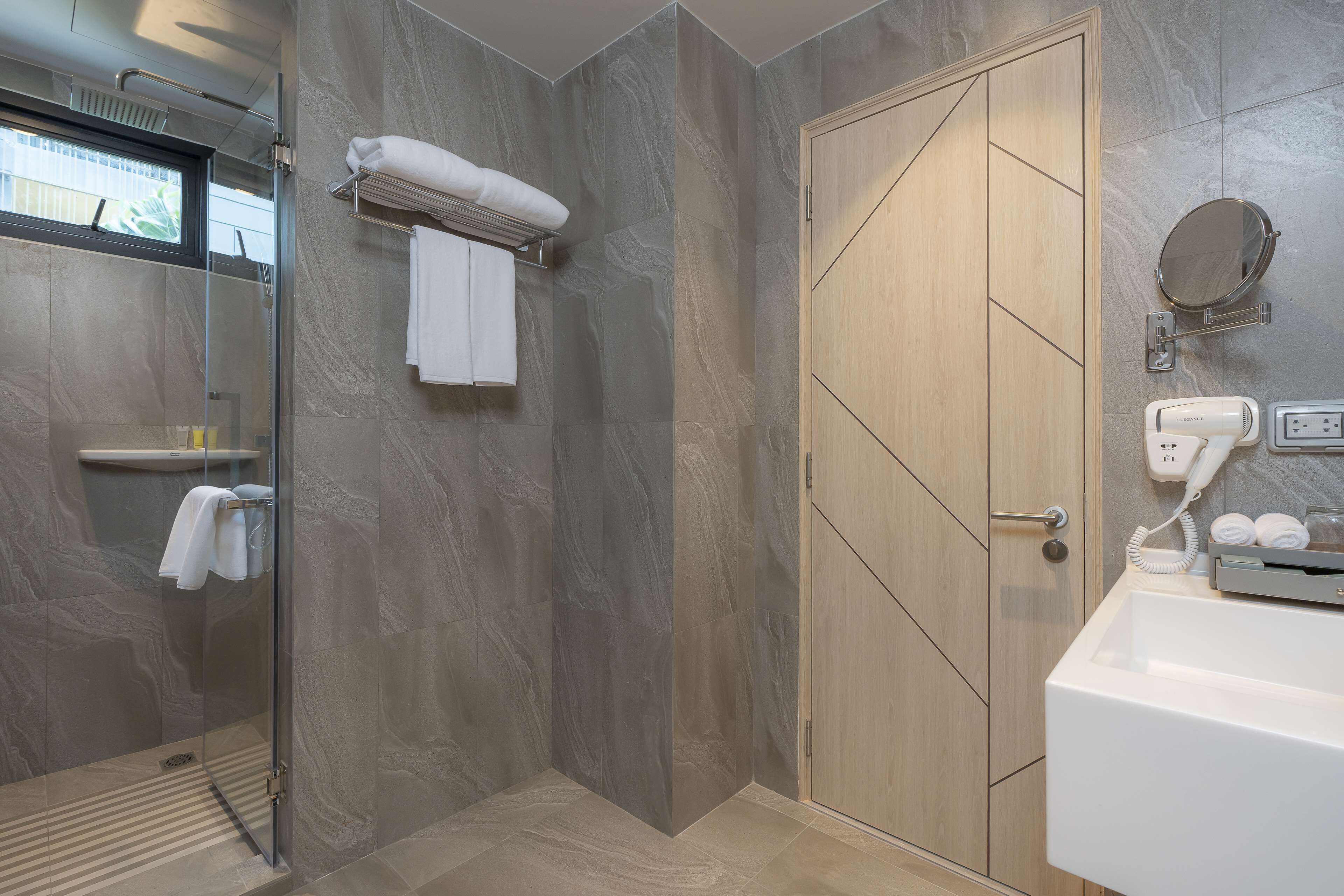 Une salle de bain moderne avec une douche à parois de verre, une porte en bois, un lavabo blanc et un porte-serviettes.