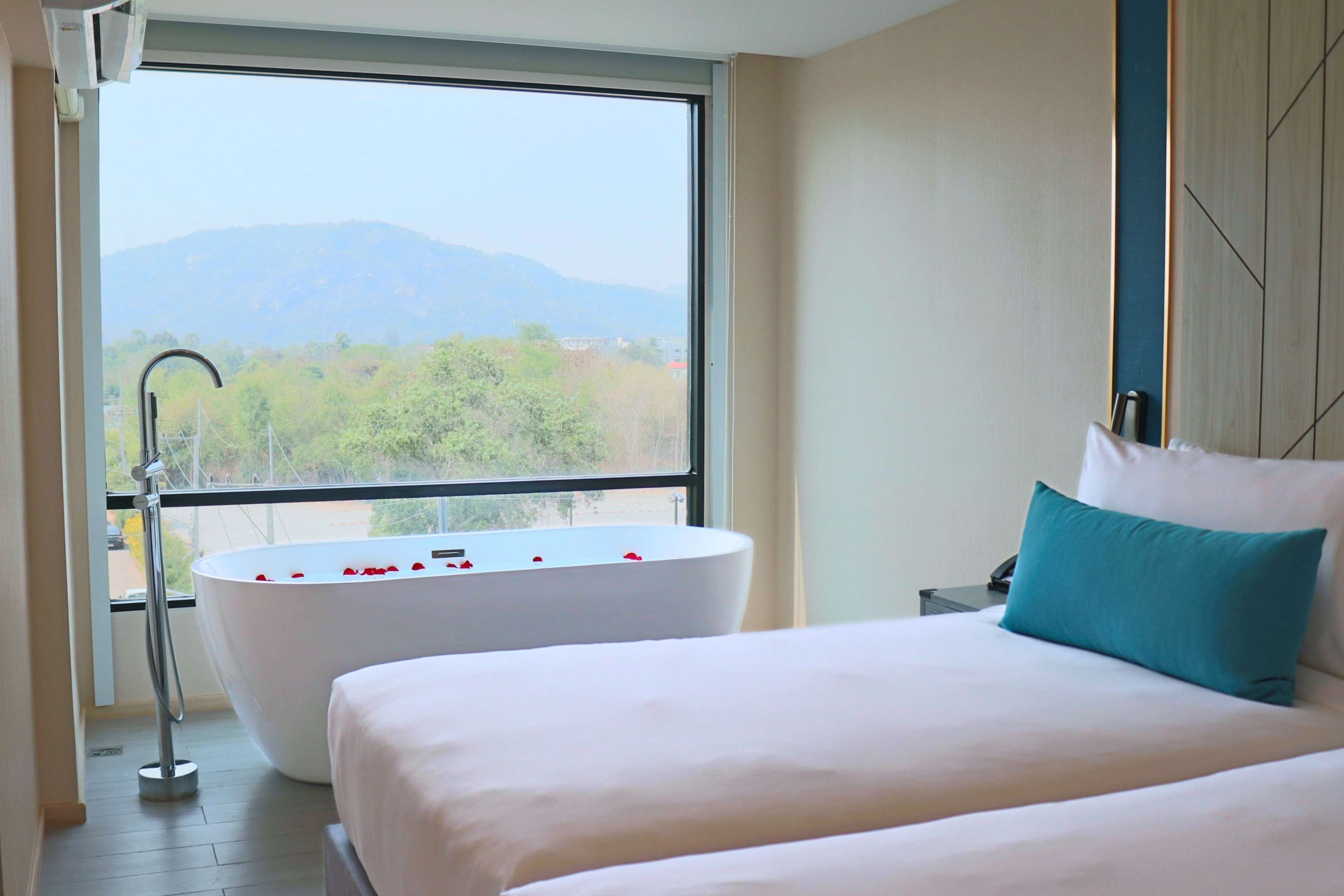A bedroom with a large bed, a bathtub filled with rose petals, and a view of mountains through a large window.