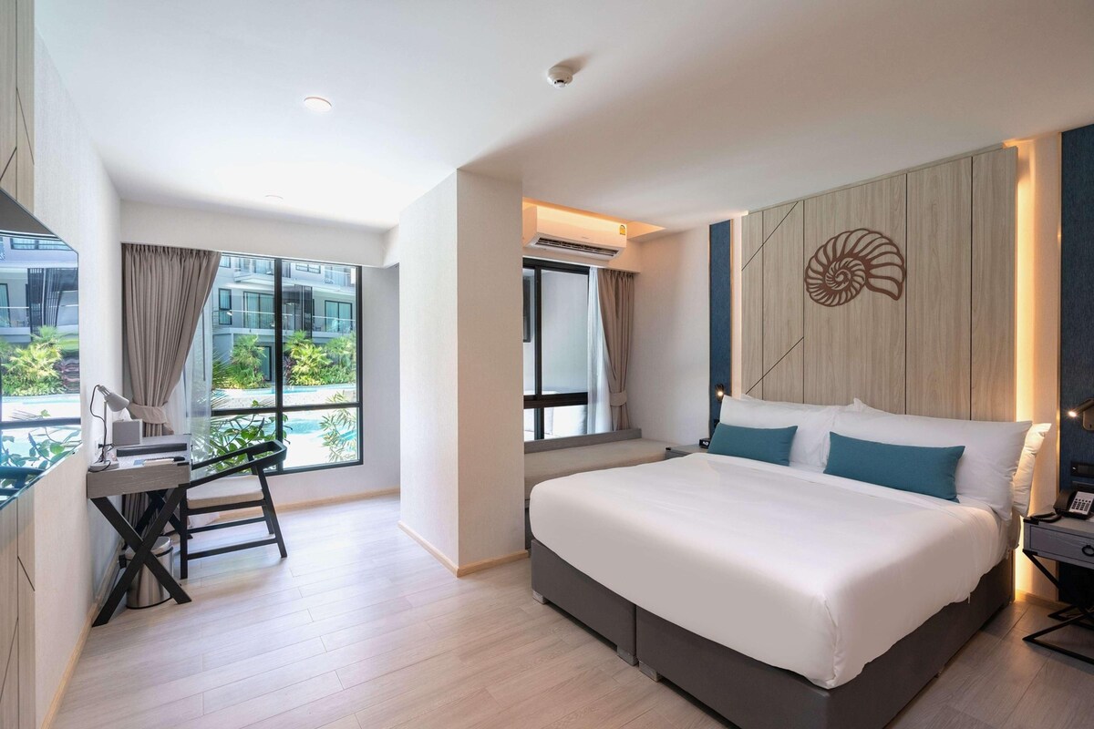 A modern hotel room with a large bed, a desk, and a view of the outdoors.