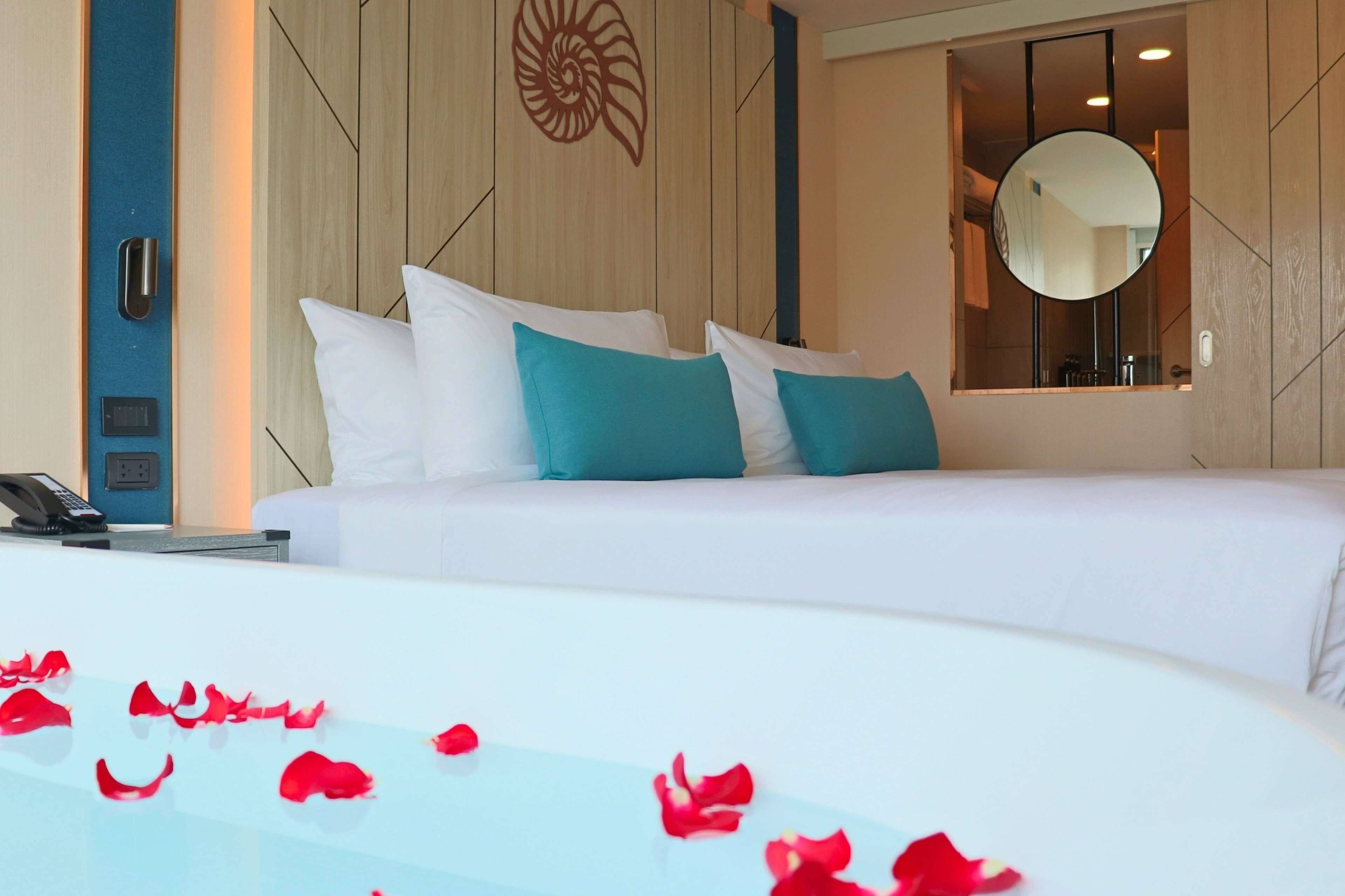 A hotel room with a bed, a bedside phone, a mirror, and a wall with a decorative design.