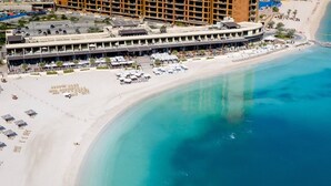 Un hotel sulla costa con una passeggiata sul lungomare, diverse aree ristorazione e un bar a bordo piscina.