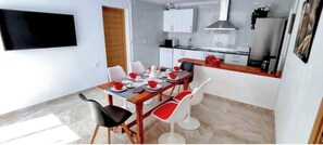 A compact kitchen with white cabinets, a stainless steel range hood, and a dining area with a wooden table and red and white chairs.