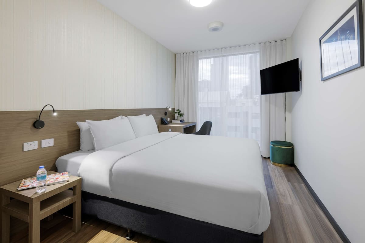 Een hotelkamer met een groot bed, nachtkastje, lamp en een flatscreen televisie aan de muur.