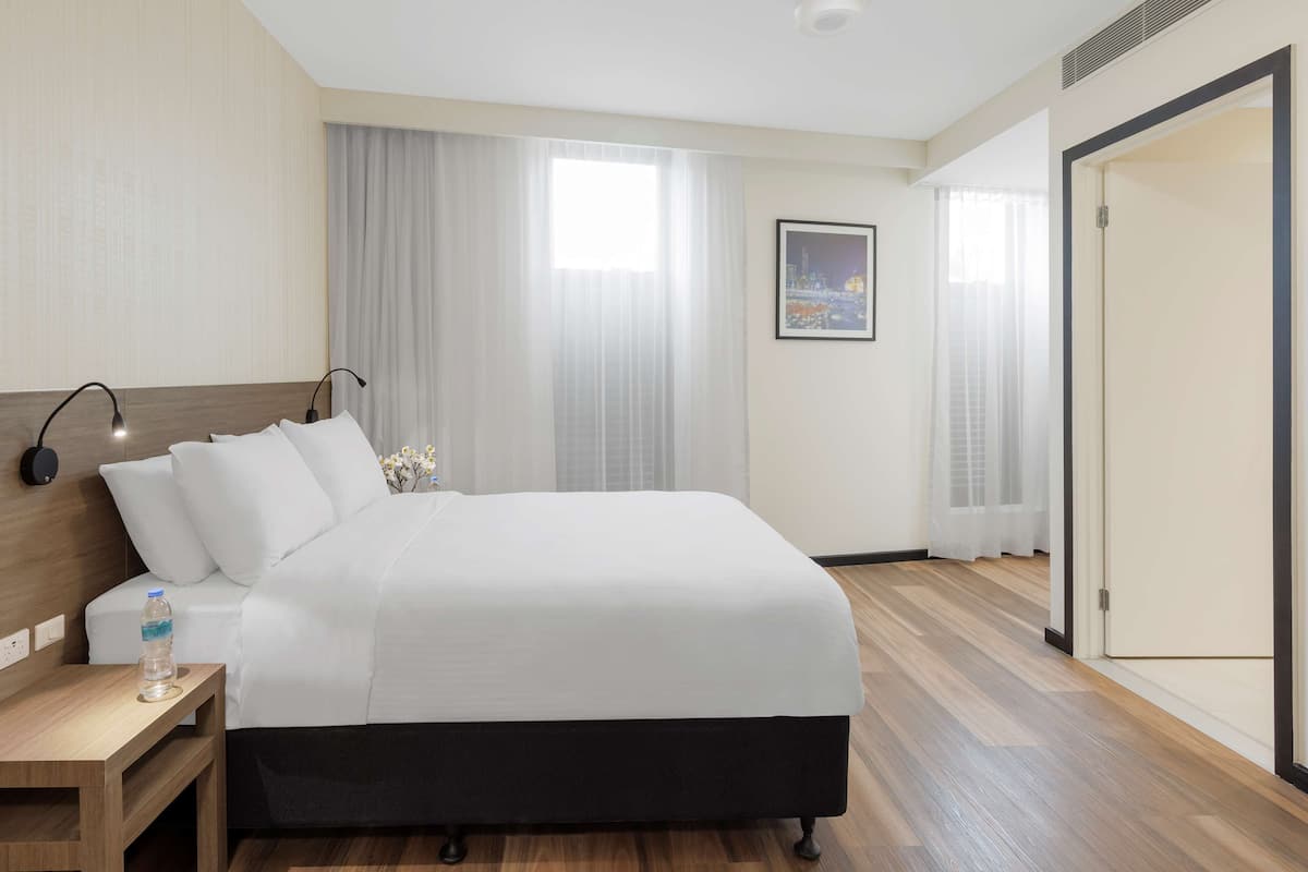 Een hotelkamer met een bed, nachtkastje, lamp en een foto aan de muur.