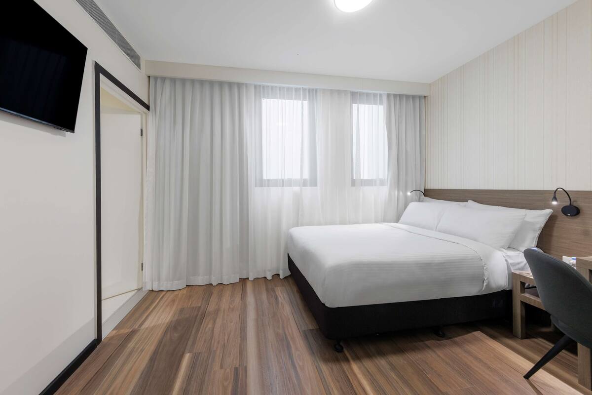 Hotelkamer met een bed, bureau, stoel, een aan de muur bevestigde televisie en een raam met gordijnen.