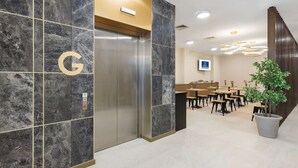 Un vestíbulo moderno con pared de mármol, un ascensor y una zona de estar con mesas y sillas.