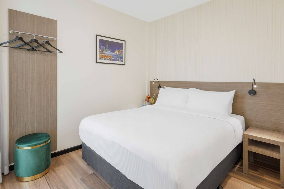 Een netjes ingerichte hotelkamer met een groot bed, een nachtkastje, een kledingrek en een kleine prullenbak.