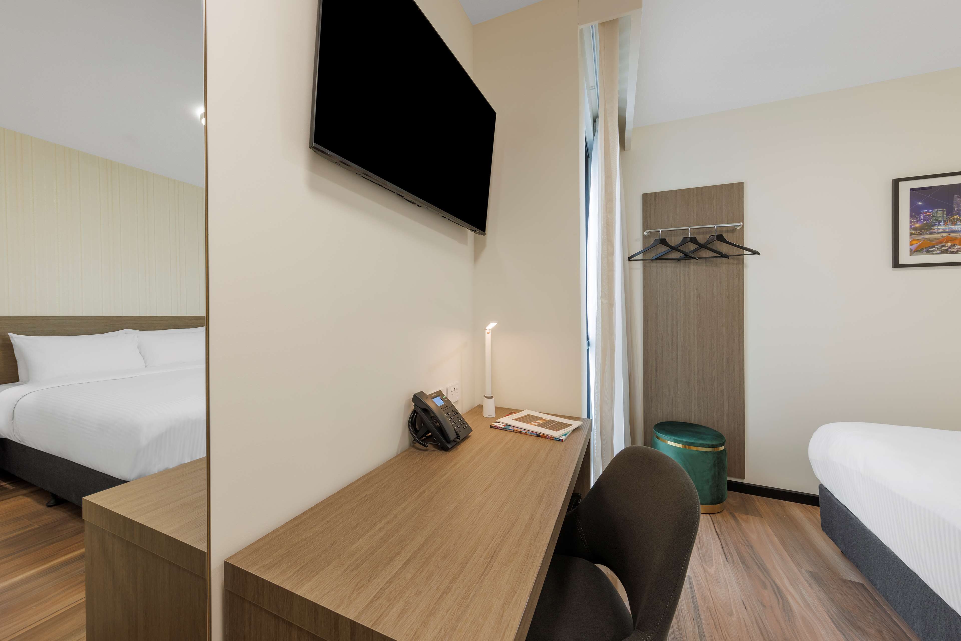 Ein Hotelzimmer mit einem Bett, einem Schreibtisch mit Telefon, einem Sessel, einem Mülleimer und einem an der Wand befestigten Fernseher.