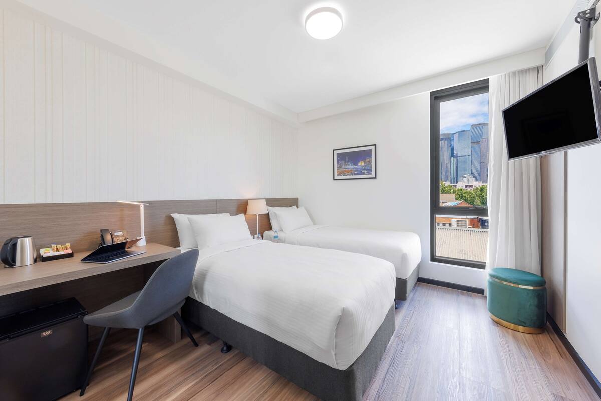 Hotelkamer met twee bedden, een bureau, een stoel, een televisie en een raam met uitzicht op de stad.
