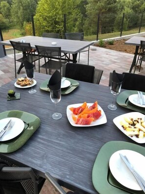 Un área de comedor al aire libre con mesas dispuestas para comidas, rodeada de sillas y vistas a árboles.