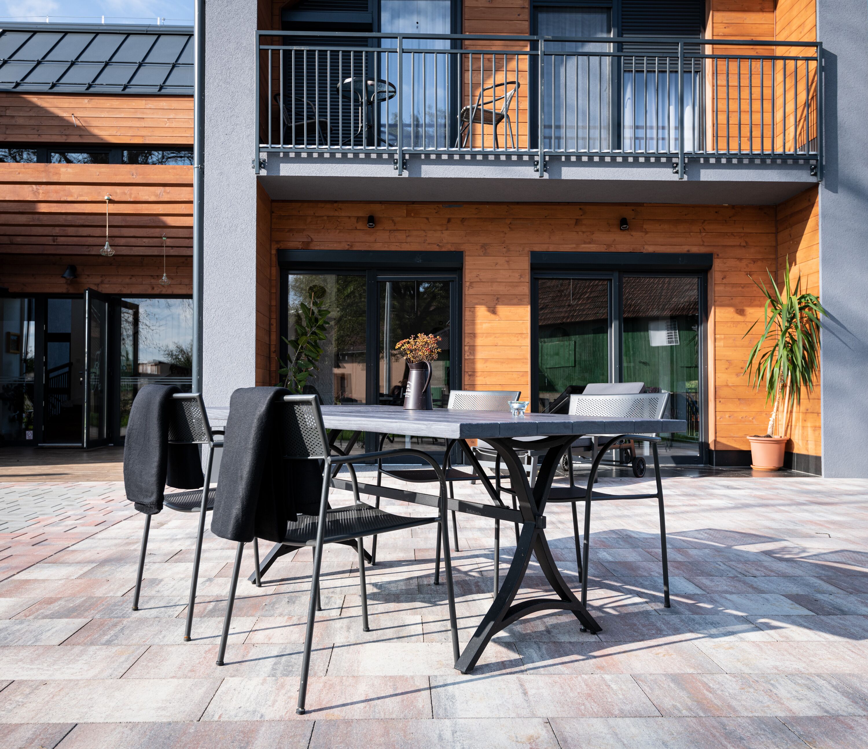 An outdoor patio with a table and chairs, a potted plant, and a balcony with a railing.