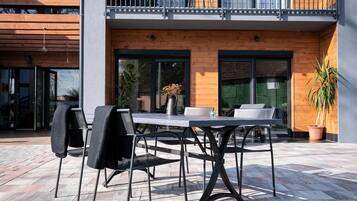 An outdoor patio with a table and chairs, a potted plant, and a balcony with a railing.