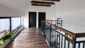 Un interior moderno con pisos de madera, un balcón con plantas y una escalera con barandilla de madera.