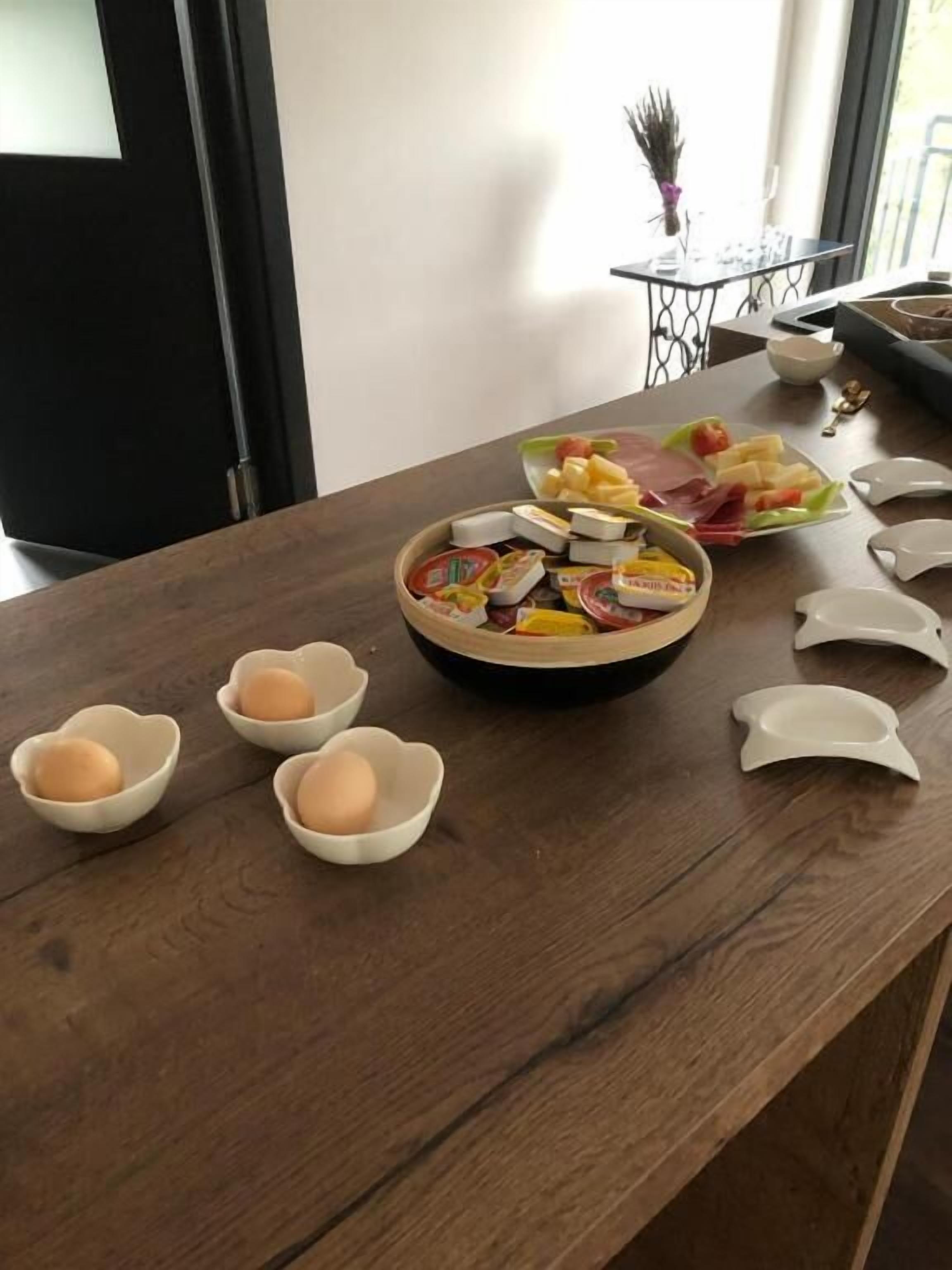Una mesa de madera con un plato de quesos variados, un bol de huevos y un pequeño florero con plantas secas.