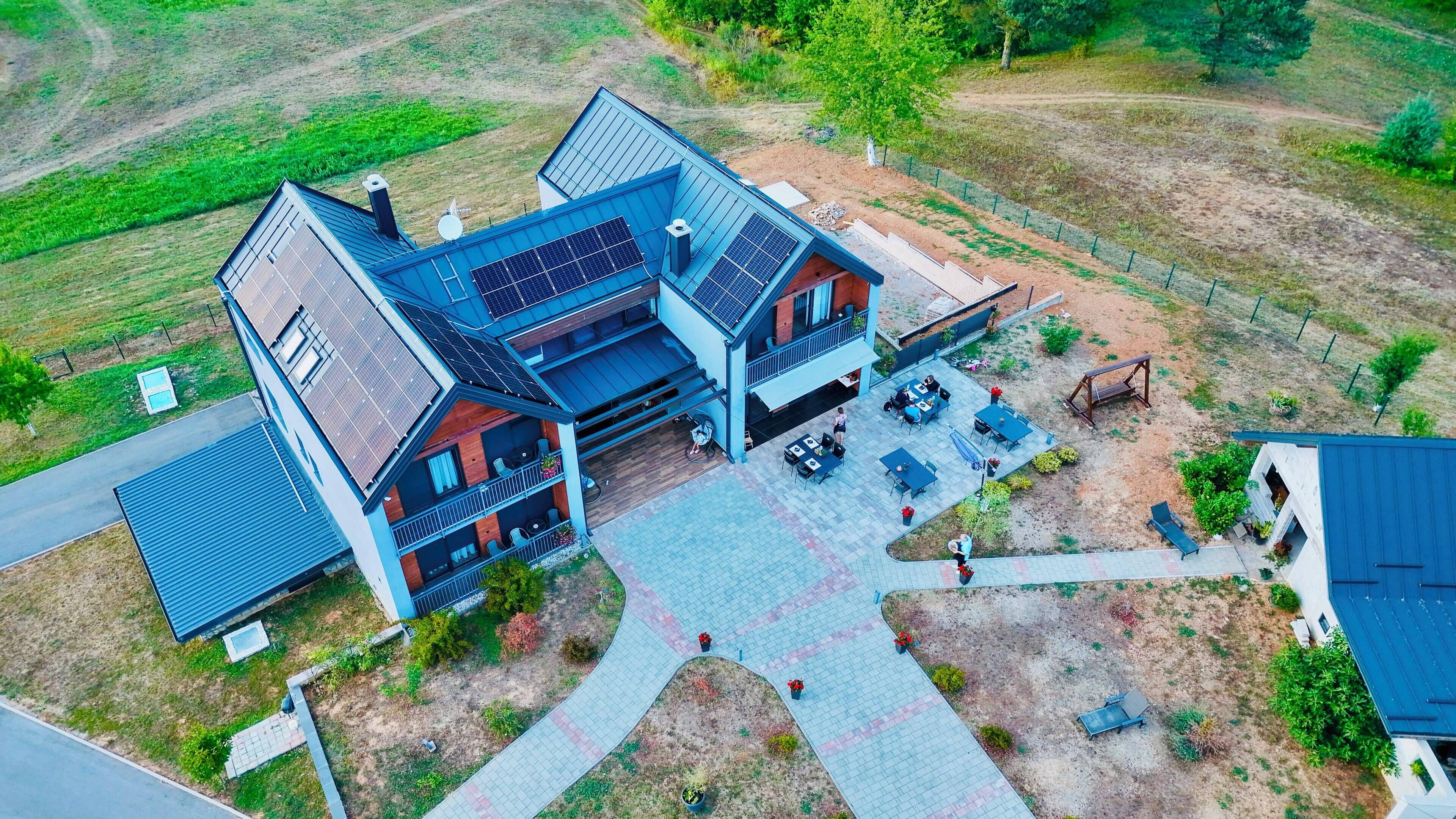 Uma casa de dois andares com um pátio, painéis solares e um quintal cercado.
