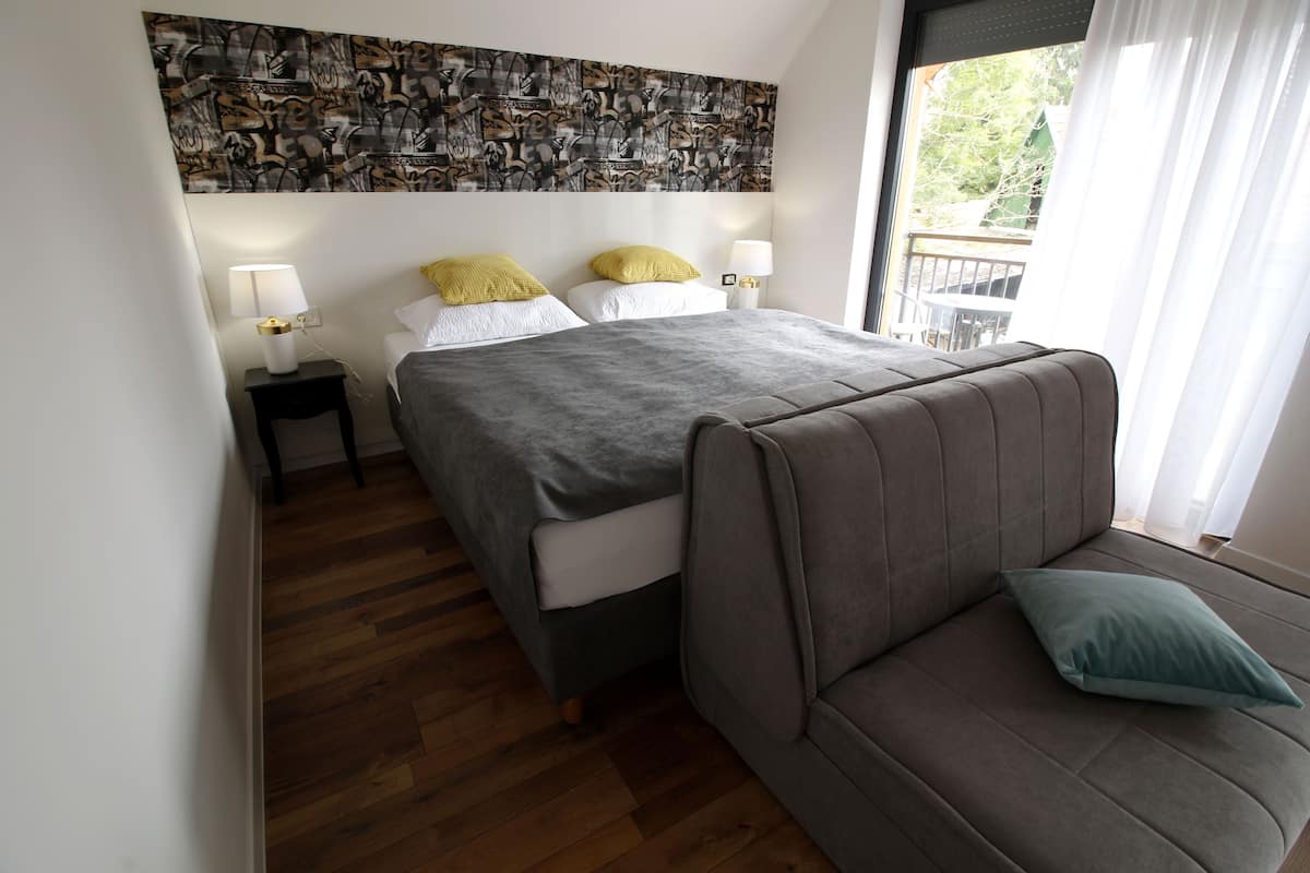 Un dormitorio con cama, dos mesitas de noche, un sofá y vistas al exterior.
