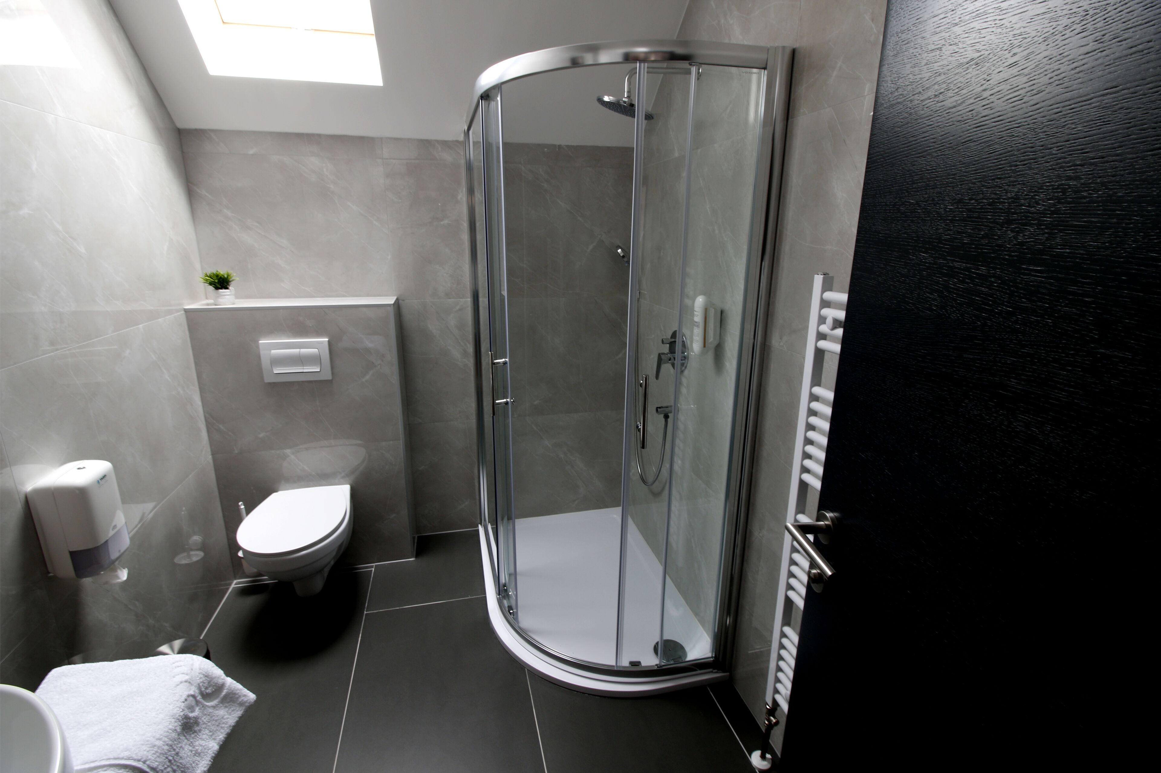 Un baño moderno con cabina de ducha de vidrio, inodoro y dispensador de jabón para manos.