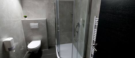 Un baño moderno con cabina de ducha de vidrio, inodoro y dispensador de jabón para manos.