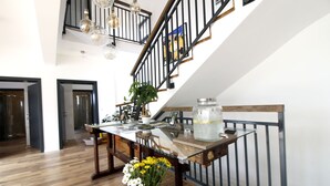 Una habitación amplia con piso de madera, una mesa de comedor con sillas, una escalera con barandilla y un candelabro.
