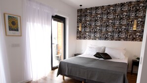Un dormitorio con una cama, un tapete blanco, suelo de madera, una ventana con cortinas, una pared con arte callejero y un cuadro enmarcado.