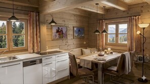 A wooden cabin interior with a kitchen, dining area, and large windows.