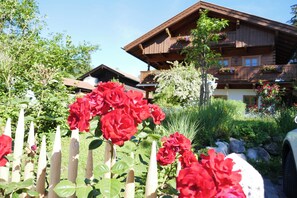Un bâtiment en bois doté de balcons, entouré d’un jardin où poussent des fleurs rouges et délimité par une clôture en bois.