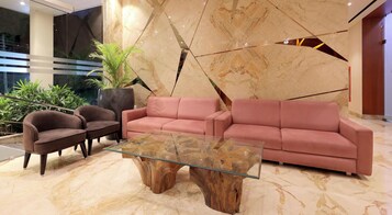Un hall d’entrée moderne avec un sol en marbre, une table basse en verre, un canapé rose et deux fauteuils sombres.