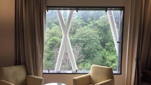 Una habitación con dos sillas, una mesita pequeña y un ventanal con vistas a un bosque.