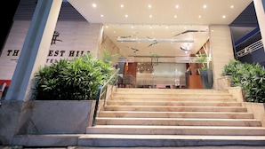 Fachada de hotel con una escalera que lleva al vestíbulo, un letrero con el nombre del hotel, y un diseño moderno con plantas e iluminación.