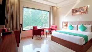 Habitación de hotel con una cama grande, un escritorio, una silla, una mesita y un ventanal con vistas a zonas verdes.
