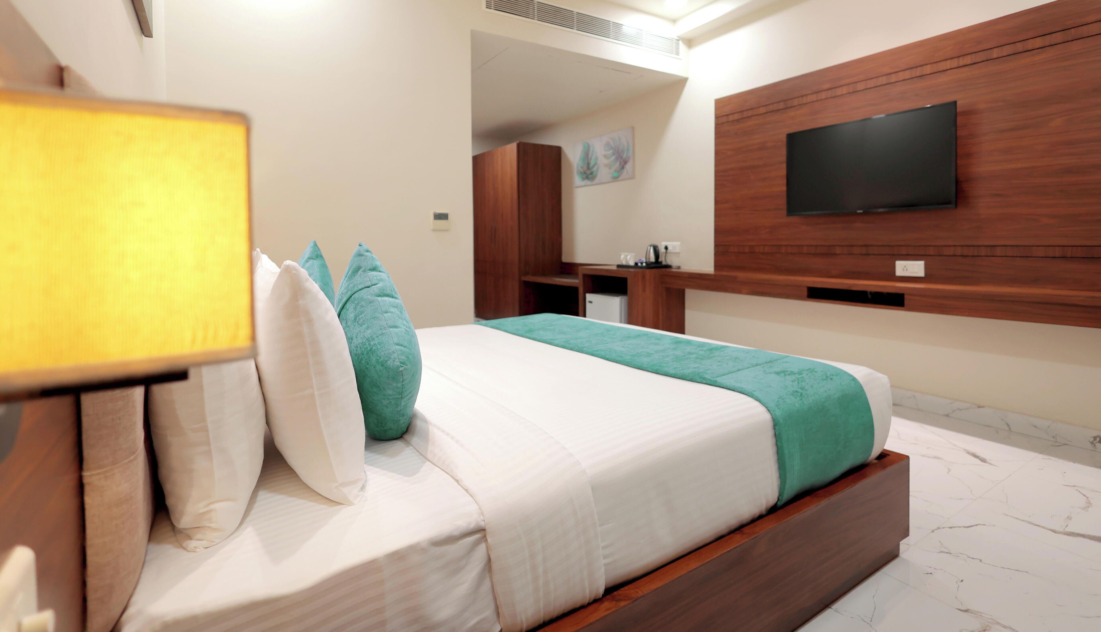 Une chambre d’hôtel moderne équipée d’un lit, d’un téléviseur fixé au mur, d’un petit bureau et d’un miroir.