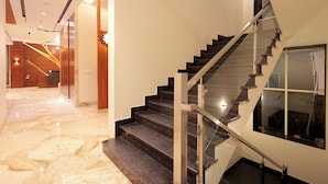 Un interior de hotel moderno con un pasillo de mármol, una escalera con barandillas de vidrio y un mostrador de recepción.